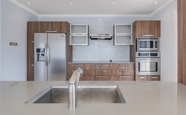 A clean contemporary ktichen, the sink in the foreground and the refrigerator and oven in the background